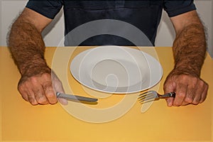 Male hands with a knife and fork are lying on the table in front of an empty white plate
