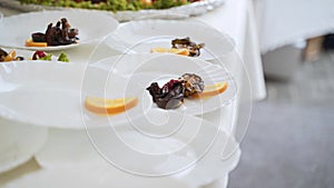 Male hands lay out grilled vegetables in white plates with culinary tongs.