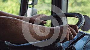 Male hands of lorry driver holds a big steering wheel while driving a truck at summer day. Trucker riding to destination