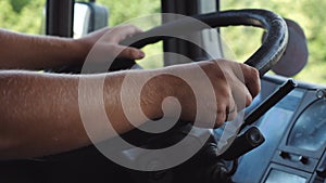 Male hands of lorry driver holds a big steering wheel while driving a truck at summer day. Trucker riding to destination