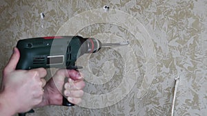 Male hands make hole using electric drill with twist drill bit