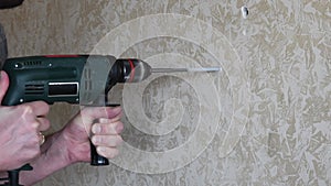 Male hands make hole using electric drill with twist drill bit