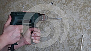 Male hands make hole using electric drill with twist drill bit