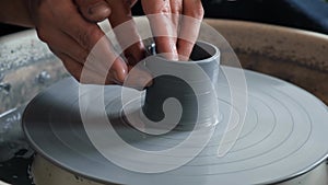 Male hands making ceramic cup on pottery wheel. Man ceramicist working with gray clay in workshop creating a mug