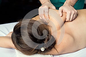 Male hands massage the muscles of the female shoulder blade and shoulder