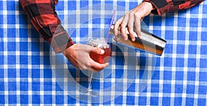 Male hands mixing drink or cocktail on checkered tablecloth