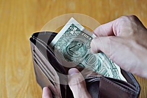 Male hands opening an almost empty leather wallet with only one American dollar (One USD, US dollar) as a symbol of modern poor pe
