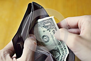 Male hands opening an almost empty leather wallet with only one American dollar (One USD, US dollar) as a symbol of modern poor pe