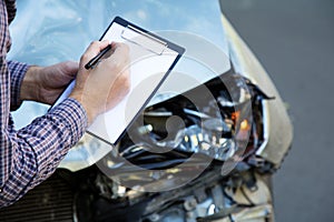 Male hands with paper mock up auto insurance blank against Destroyed car in car crash traffic accident on road. Smashed