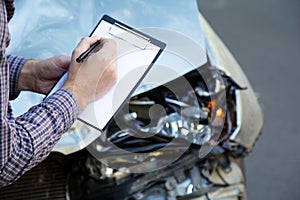 Male hands with paper mock up auto insurance blank against Destroyed car in car crash traffic accident on road. Smashed broken