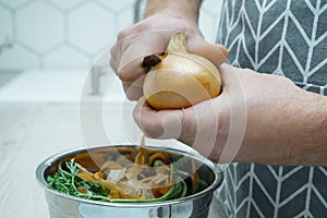 Male hands peeling by knife yellow onion over bowl of vegetable peelings closeup. Healthy nutrition, vegetables.
