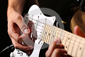 Male hands playing electric guitar with plectrum closeup