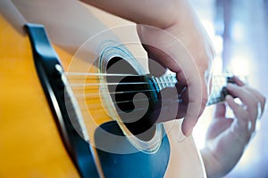 Male hands playing fingers style on a western dreadnought guitar in blue neon light