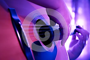 Male hands playing fingers style on a western dreadnought guitar in purple neon light.