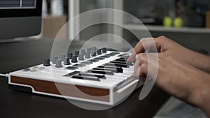 Male hands playing midi keyboard with pads on table in home studio