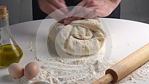 Male hands pour flour on dough and kneading dough. Closeup shot of chef making pizza dough on table