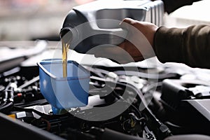Male hands pouring machine oil through funnel into car engine