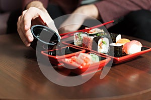 Male hands pours sauce in a plate. Sushi set