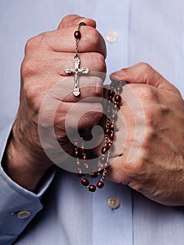 Male hands praying holding a rosary with Jesus Christ in the cross or Crucifix on black background.