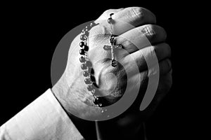 Male hands praying holding a rosary with Jesus Christ in the cross or Crucifix on black background.