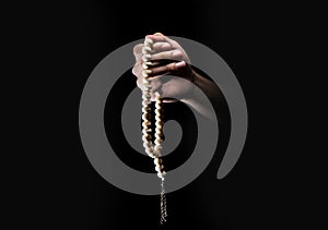 Male hands praying using prayer beads over dark backgroud