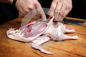 male hands prepare a raw duck to get the breast fillet for cooking on a rustic wooden butcher block