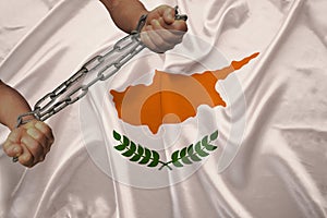 Male hands of a prisoner in iron chains against the background of the national flag of cyprus on a beautiful silk fabric, the