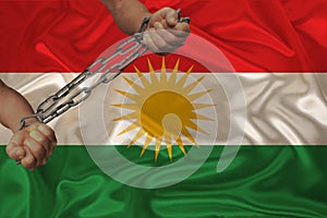 Male hands of a prisoner in iron chains against the background of the national flag of kurdistan, rojava, concept of political