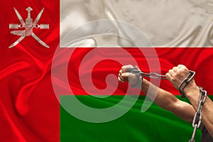 Male hands of a prisoner in iron chains against the background of the national flag of Oman on a beautiful silk fabric, the