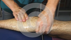 Male hands of professional masseur healing massaging foot of young sportsman with oil in parlor. Arms of massagist doing