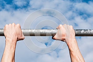 Male hands during a pull-up workout on the bar outdoors