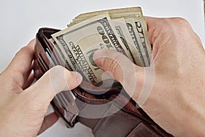 Male hands pulling a pile of American bank notes USD currency, US Dollars from a leather wallet