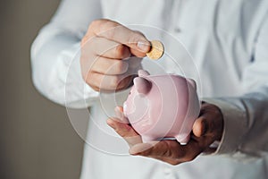 Male hands put a coin in a pink piggy bank. The concept of saving money or savings, investment. world crisis