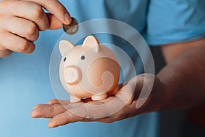 Male hands put a coin in a pink piggy bank. The concept of saving money or savings, investment. world crisis