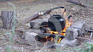 Male Hands Puts an Old Smoke Black Teapot on a Bonfire in Wood. 4K. Close up