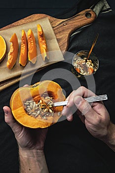 Male hands removing seeds with spoon from a fresh cut pumpkin on black background