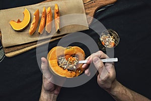 Male hands removing seeds with spoon from a fresh cut pumpkin on black background