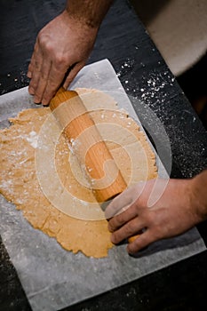 male hands roll gingerbread dough with a wooden rolling pin, close-up