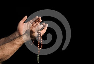 Male hands with rosary beads on black background