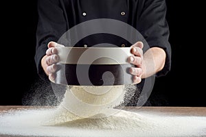 Male hands sifting flour from old sieve on old wooden kitchen table. on black background.