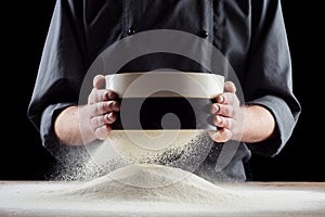 Male hands sifting flour from old sieve on old wooden kitchen table. on black background.