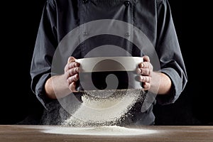 Male hands sifting flour from old sieve on old wooden kitchen table. Isolated on black background.