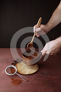 Male hands stirs melted chocolate swirl in pan on the wooden background