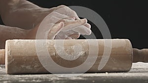 Male hands take off small piece of baking dough from the flour sprinkled table after rolling out and crumple it.