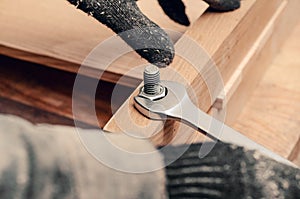 Male hands tighten the nut on the thread of the bolt screwed into the wooden structure