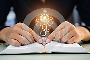 Male hands touching to light bulb which have mechanical gear inside on open book for creative thinking of problem solving and