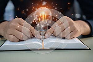 Male hands touching to light bulb which have mechanical gear inside on open book for creative thinking of problem solving and