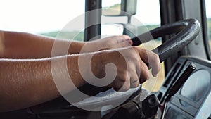 Male hands of trucker holds a big steering wheel while operating a truck through countryside. Lorry driver riding to