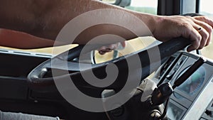 Male hands of trucker holds a big steering wheel while operating a truck through countryside. Lorry driver riding to