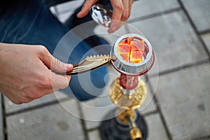 Male hands with tweezers and metal cap near hookah